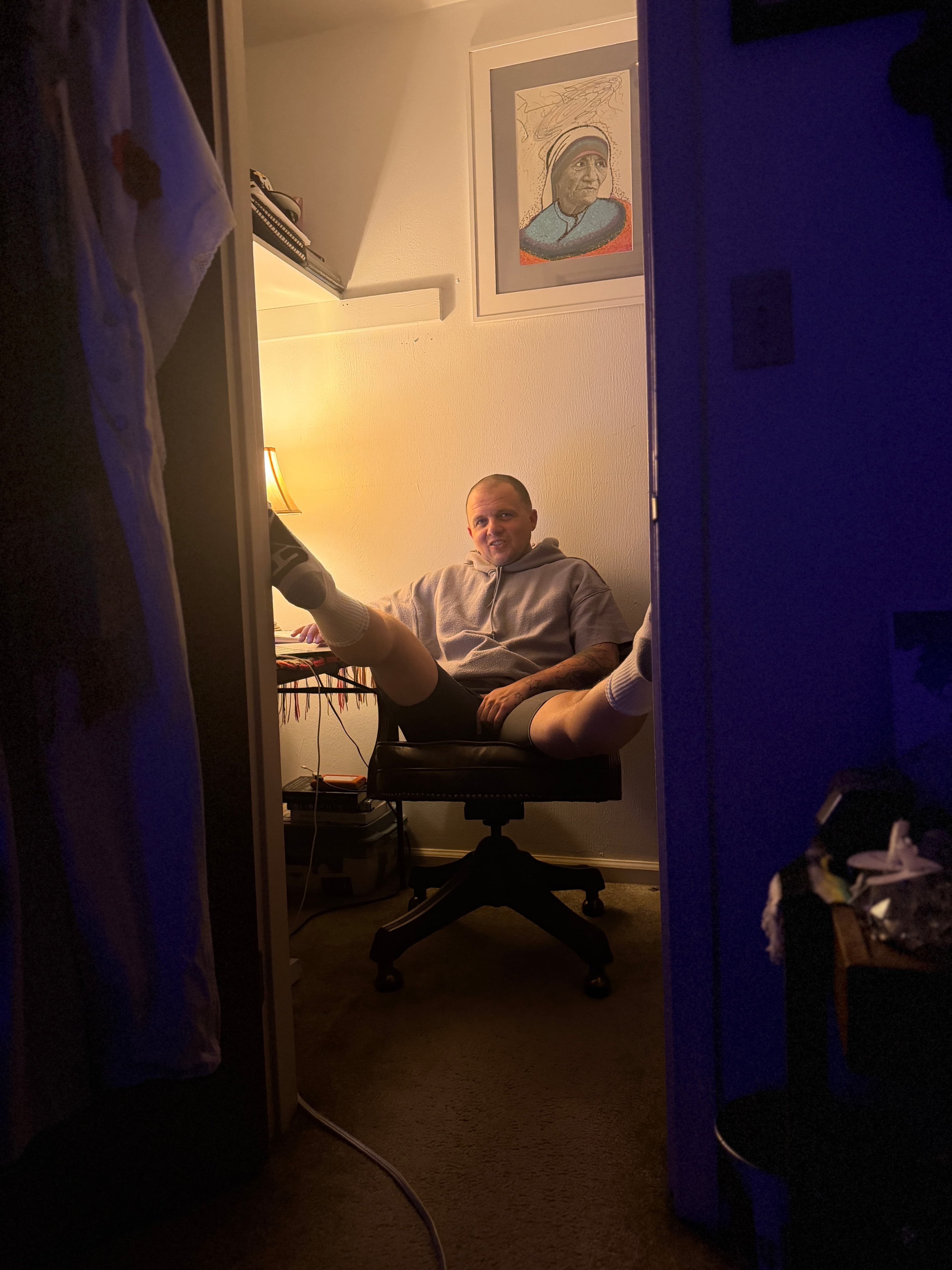 Benjamin coding at a desk in headphones, lit by a single lamp, working on the laptop in the closet