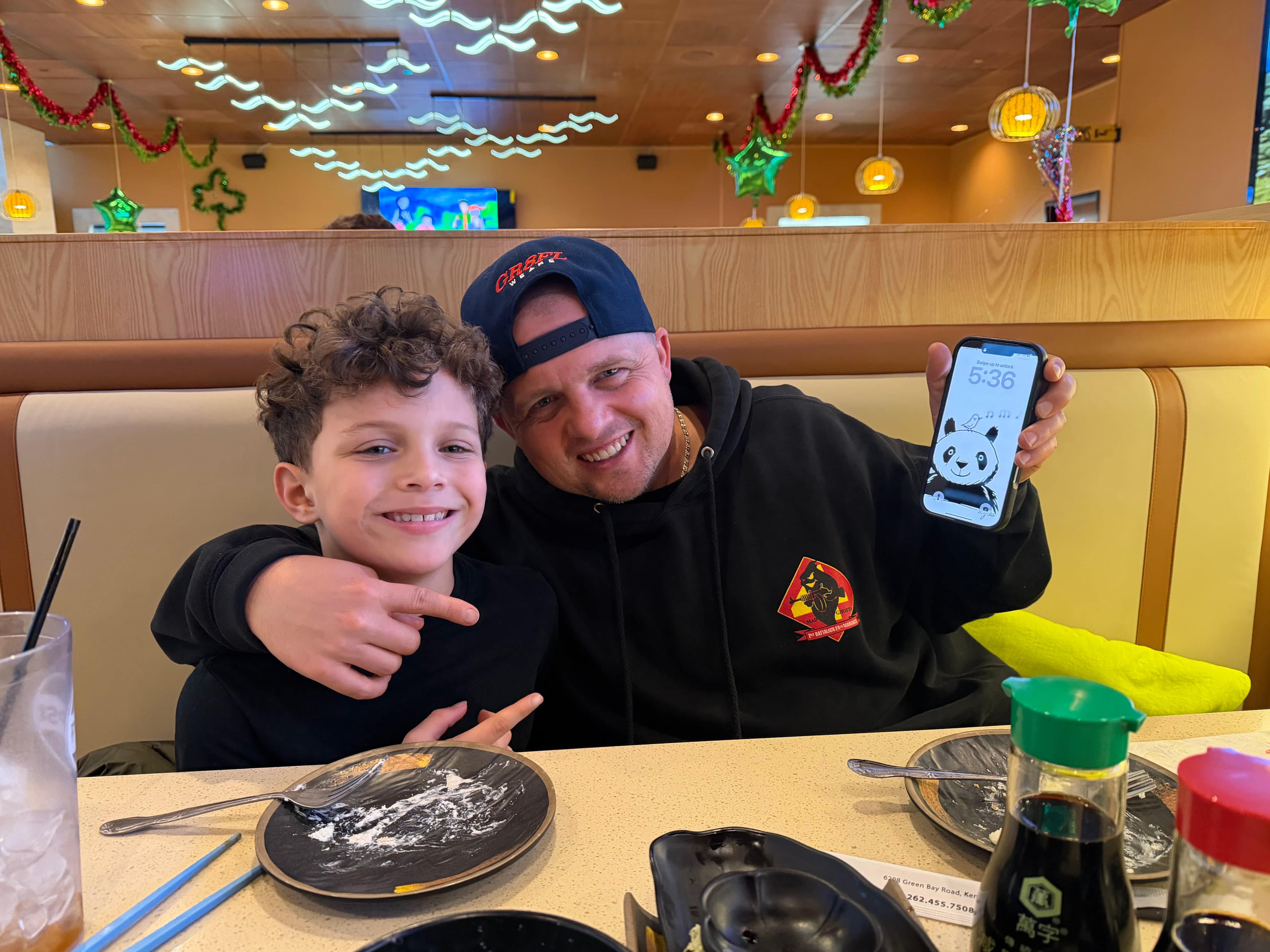 Benjamin and Myles in a sushi restaurant booth, Myles holding a phone showing the panda lock screen