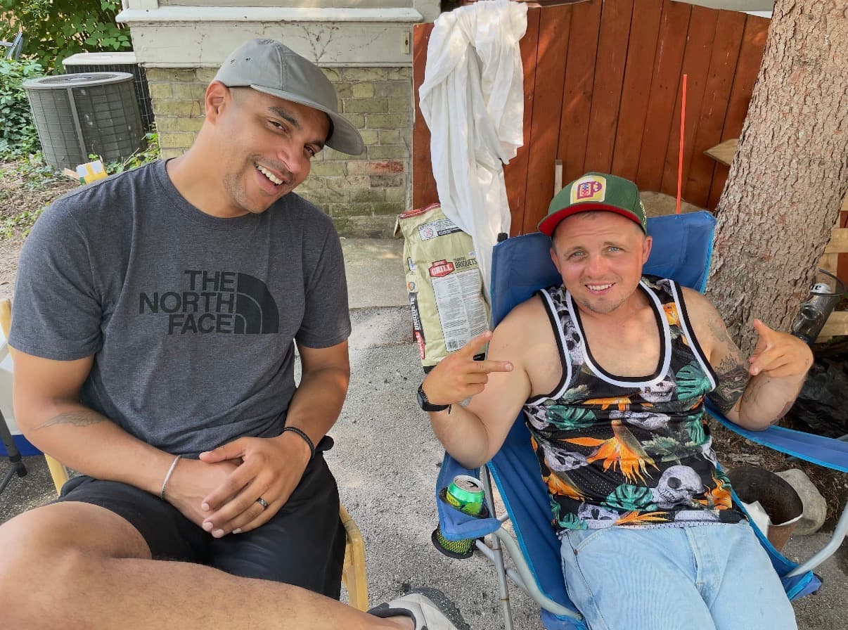 Benjamin and Steven sitting in lawn chairs in a Milwaukee backyard, both smiling, Steven pointing finger guns at the camera